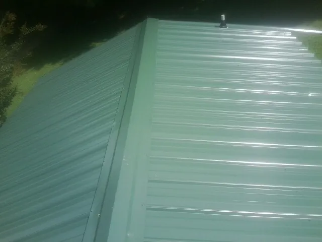 New green metal panels meeting at the ridge of a roof — Flat Roof Repair work by our crew in West Point